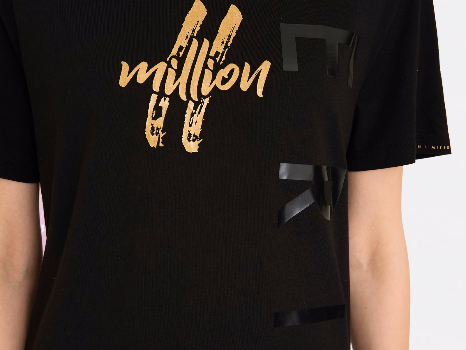 Nærbillede af en grafik i guldfolie ved siden af et ton-i-ton-tryk på en sort T-shirt
