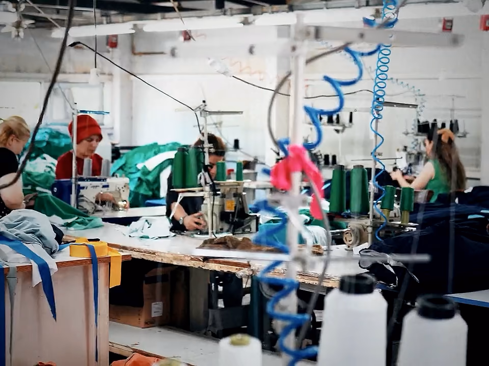Vista d'insieme del reparto cucito, con file di macchine, coni di filo e capi in lavorazione