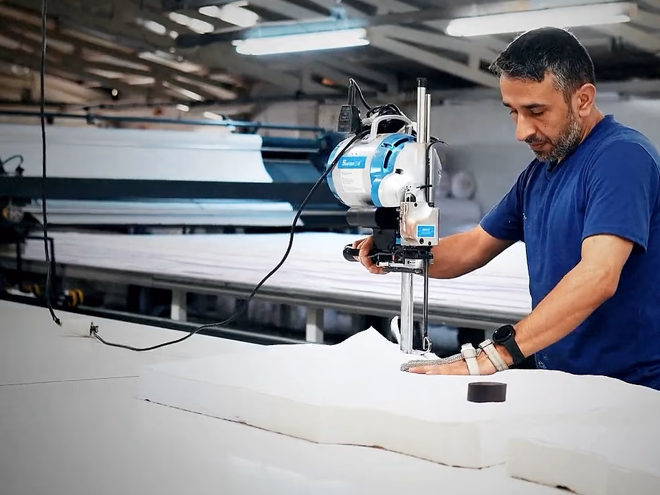 Beyaz kumaş serimini dik bıçaklı kesim makinesiyle kesen operatör